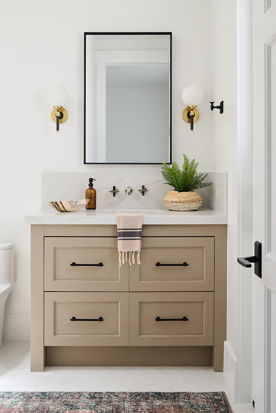 Bathroom with tan vaniry, cool gold and black sconecs and back framed rectangular mirror