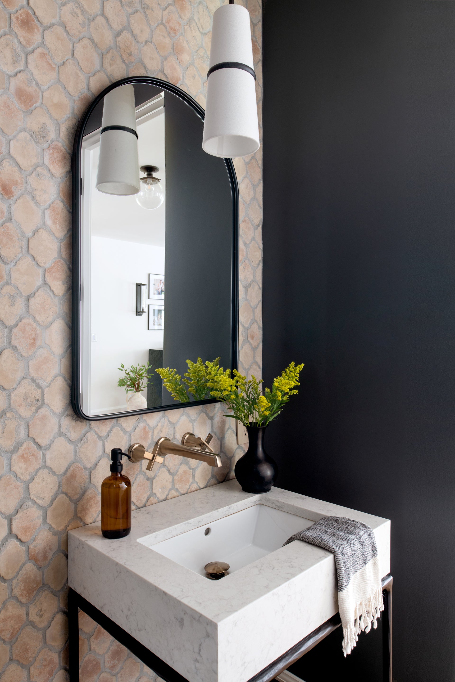 Small bathroom with terracotta tiled wall and gold in wall faucet and black rimmed, arched mirror