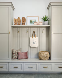 Cream mudroom cabinetry with stylish decor like a set of 3 wooden face sculpturess