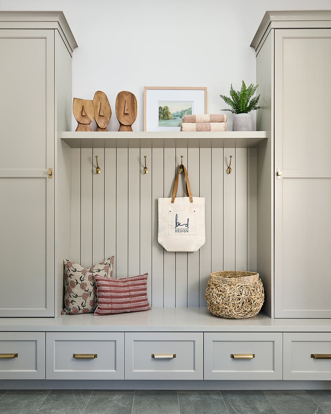 Cream mudroom cabinetry with stylish decor like a set of 3 wooden face sculpturess