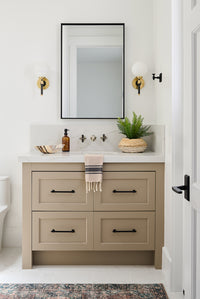 Bathroom with tan vaniry, cool gold and black sconecs and back framed rectangular mirror 