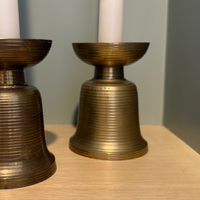 Two brass candle holders with white candles on a wooden surface.