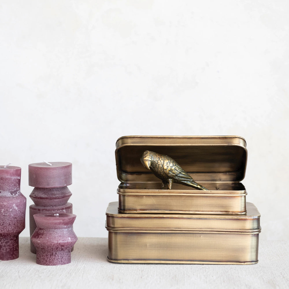 Bronze storage tin with a decorative bird on a white background. 3 Plum color pillar candles next to them