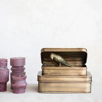 Bronze storage tin with a decorative bird on a white background. 3 Plum color pillar candles next to them