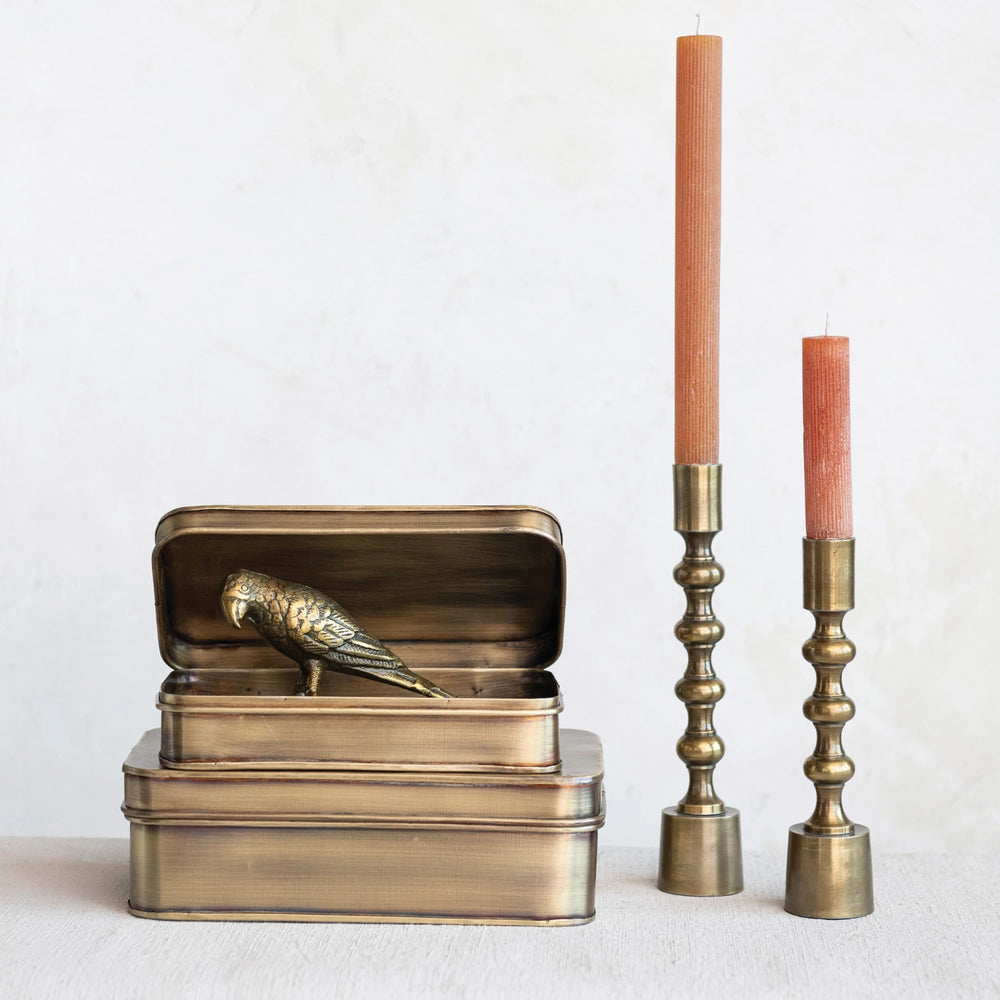 Bronze bird figurine on a box with two brass candle holders and candles on a white background