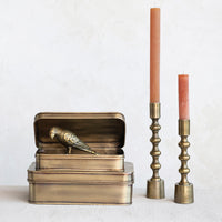 Bronze bird figurine on a box with two brass candle holders and candles on a white background