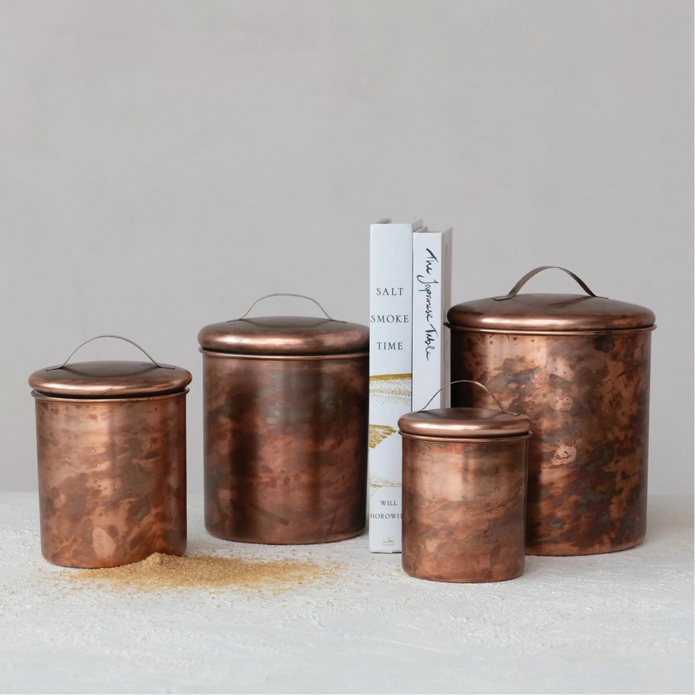 4 copper canisters of different sizes on a textured background with 2 upright books