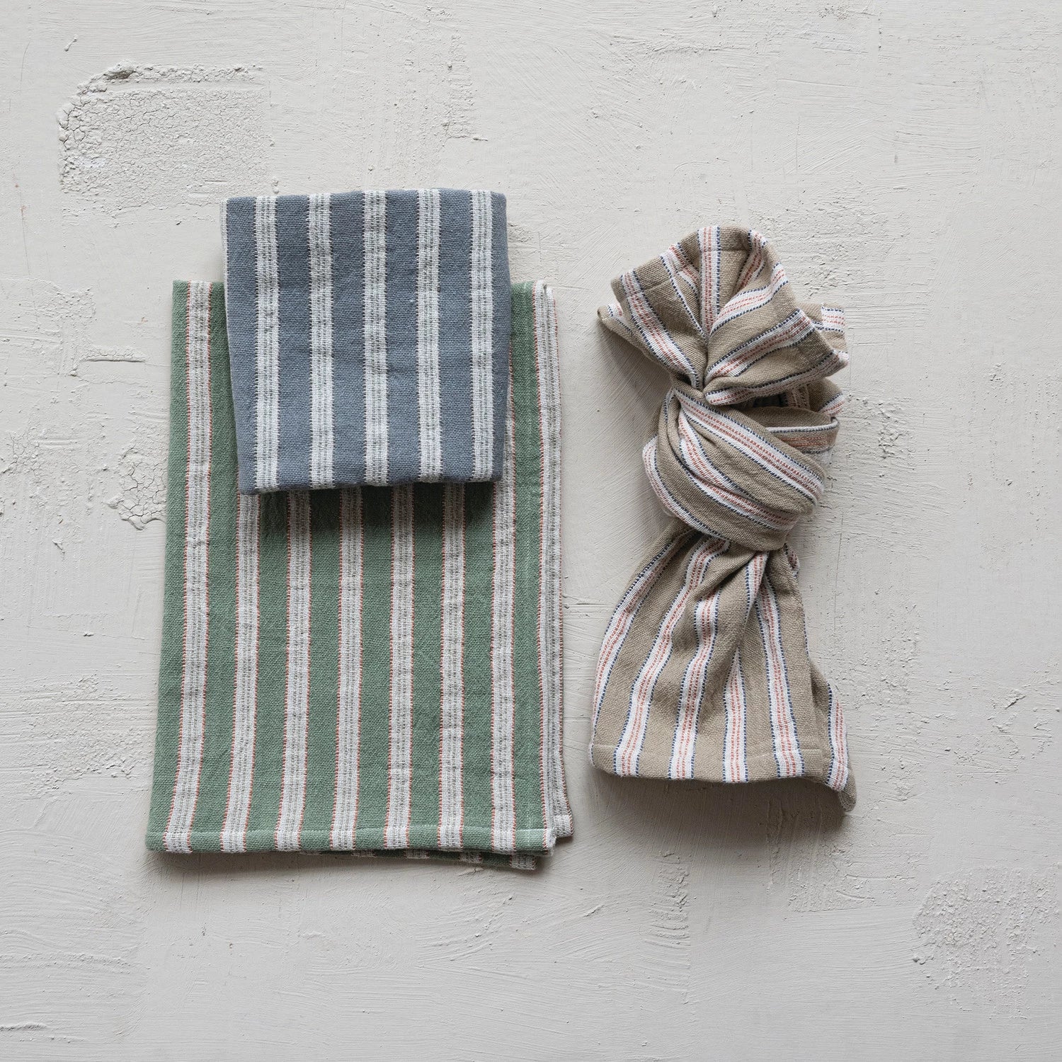 three striped fabric items on a light gray surface. the towels are green, blue, and natural color