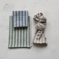 three striped fabric items on a light gray surface. the towels are green, blue, and natural color