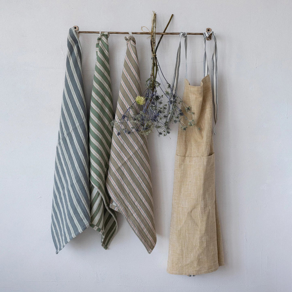 Set of striped towels and a beige apron hanging on a rack against a white wall.