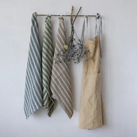 Set of striped towels and a beige apron hanging on a rack against a white wall.