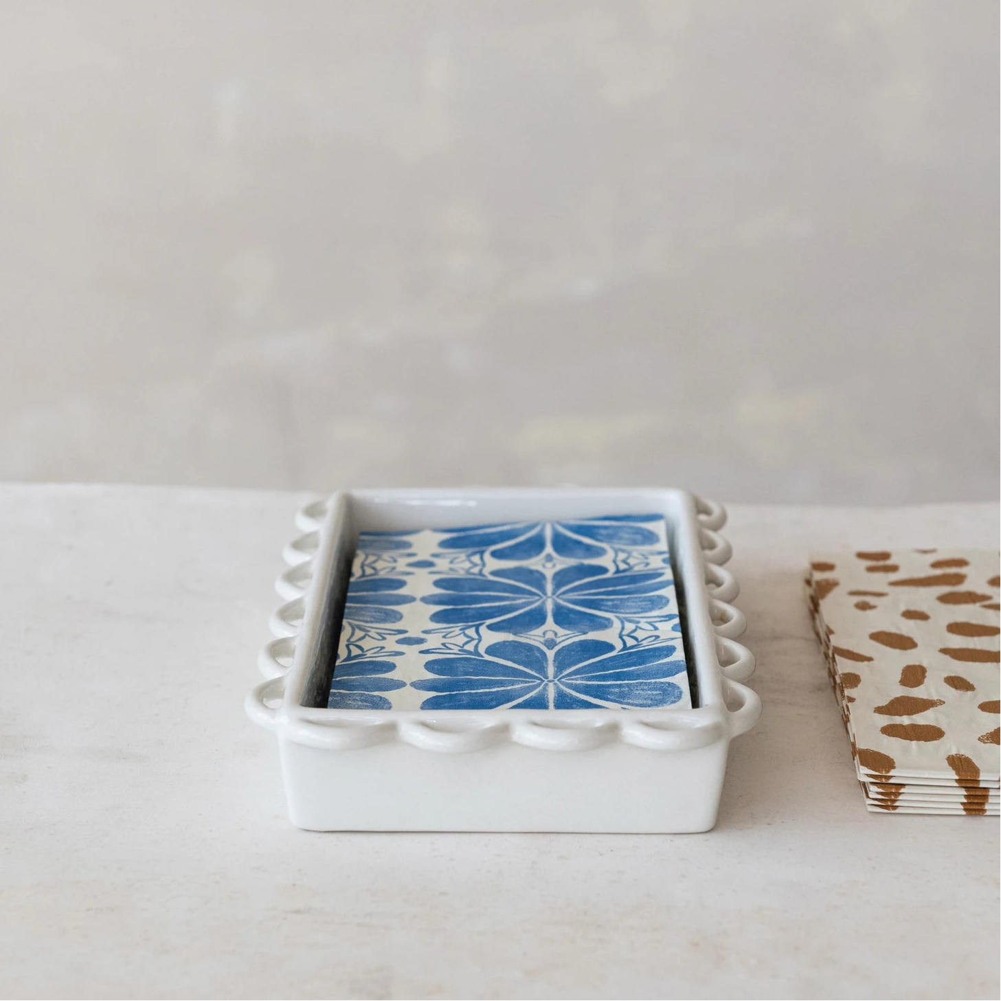 Set of napkins with blue and white design in a white holder with scallop edges on a light surface.