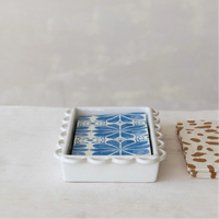 Set of napkins with blue and white design in a white holder with scallop edges on a light surface.