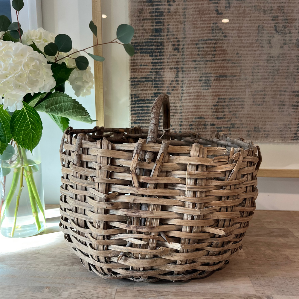 Woven basket on a wooden floor with a vase of flowers in the background