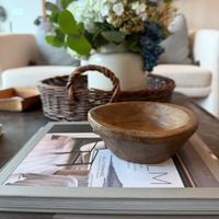 Wooden bowl on a magazine with a flower arrangement in the background