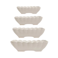 Set of four white ceramic bowls with scalloped edges on a white background