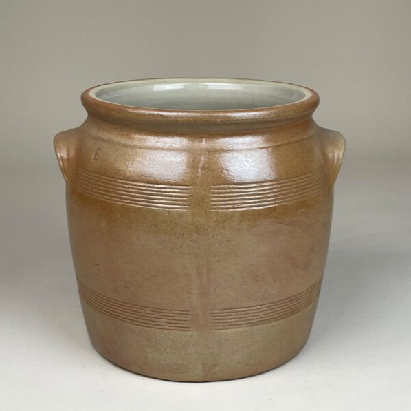 Brown ceramic jar with subtle horizontal line patterns and two small handles on either side, set against a plain background.