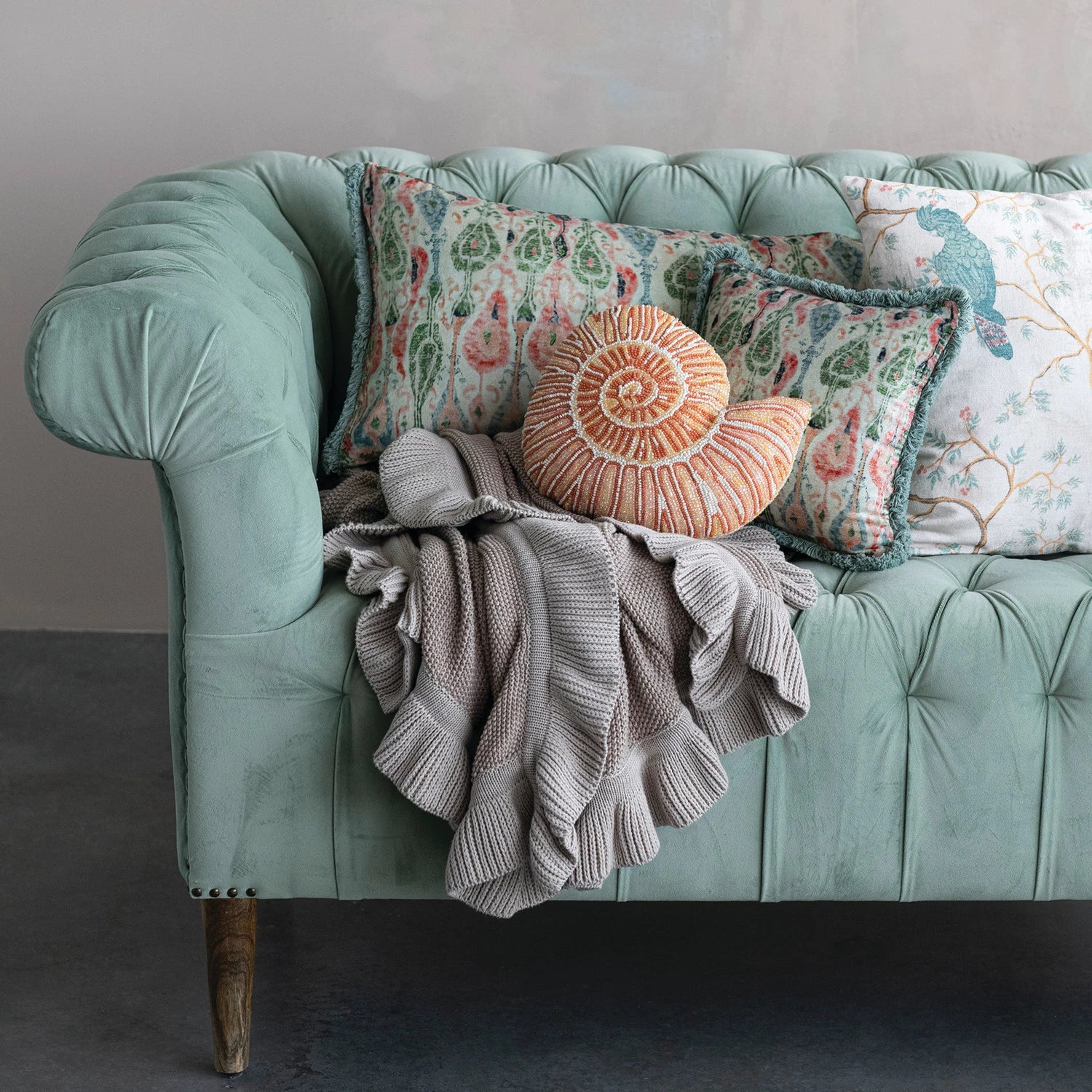 Light green sofa with decorative pillows and a blanket against a gray wall.