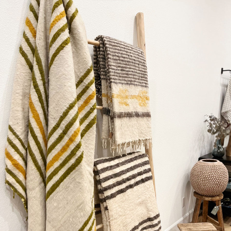 3 oatmeal colored blankets with stripes hung on a wooden ladder
