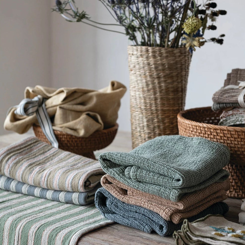 multiple Stacks of folded towels on a wooden surface with a vase of dried flowers in the background.