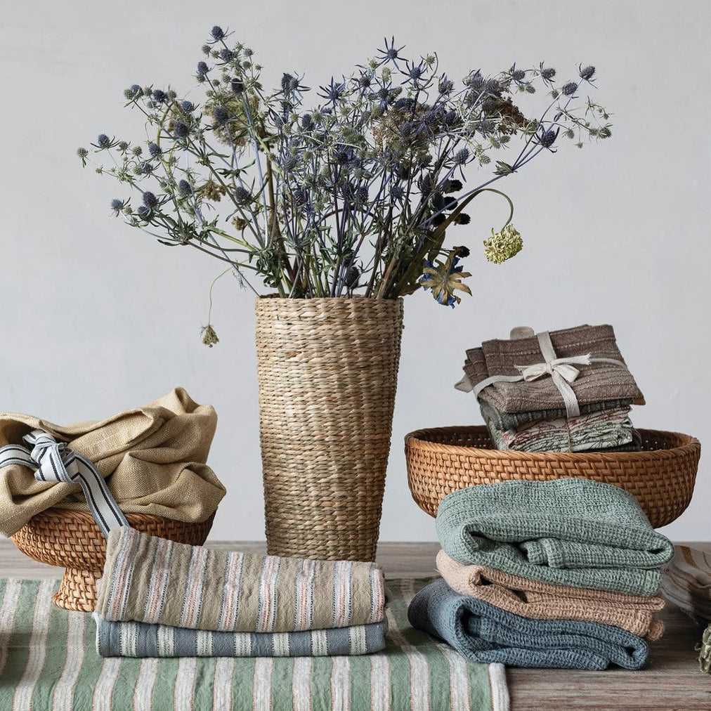 Decorative setting with folded cloths, a vase with flowers, and a striped table runner on a wooden surface.