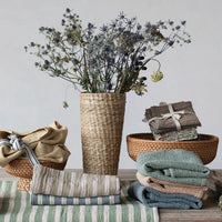 Decorative setting with folded cloths, a vase with flowers, and a striped table runner on a wooden surface.