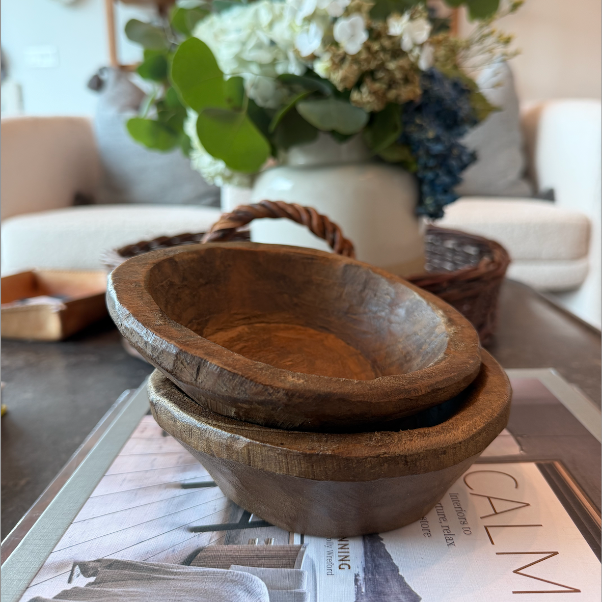 Stack of wooden bowls on a magazine with a blurred background of a living room.