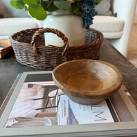 Wooden bowl on a magazine with a wicker basket in the background